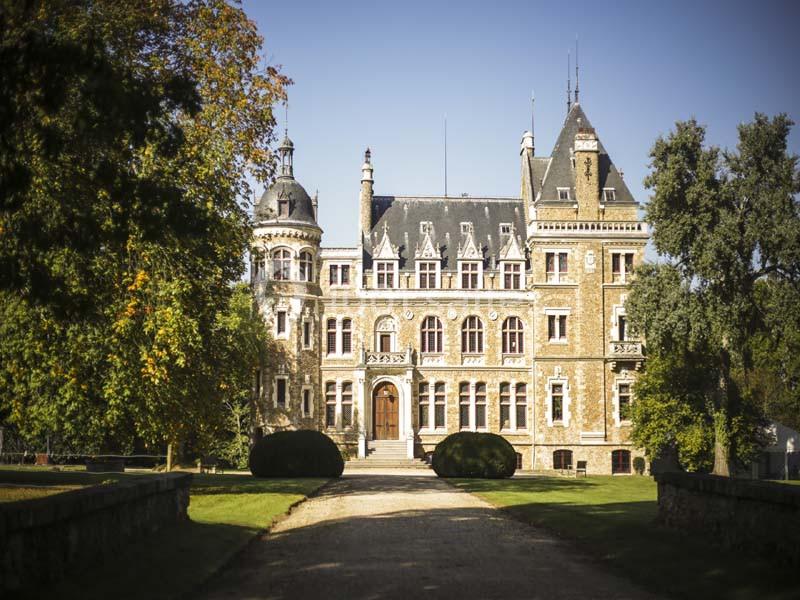 Façade d'un château en pierre entouré de verdure, avec une allée centrale menant à l'entrée principale.