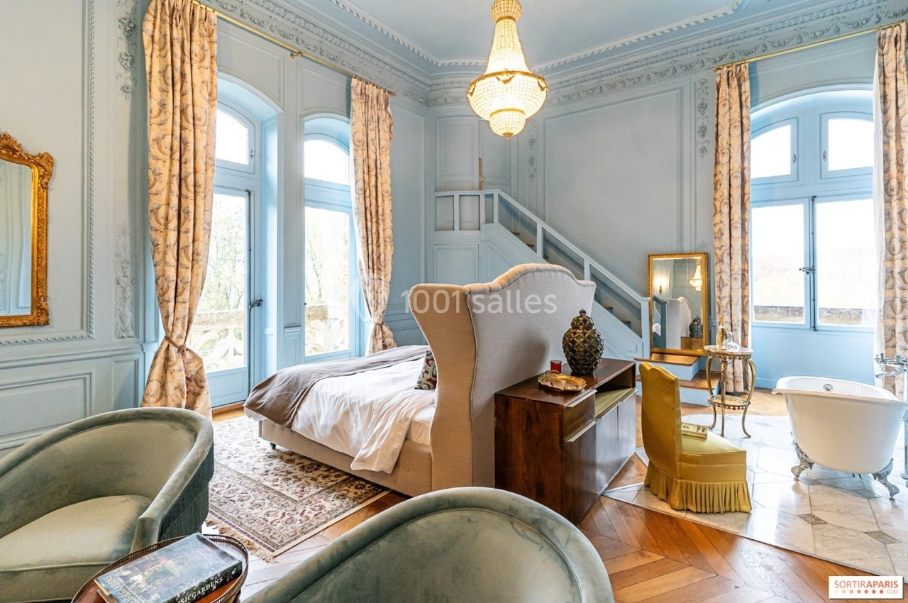 Chambre élégante avec lit double, baignoire sur pieds, fauteuils et grandes fenêtres laissant entrer la lumière naturelle.