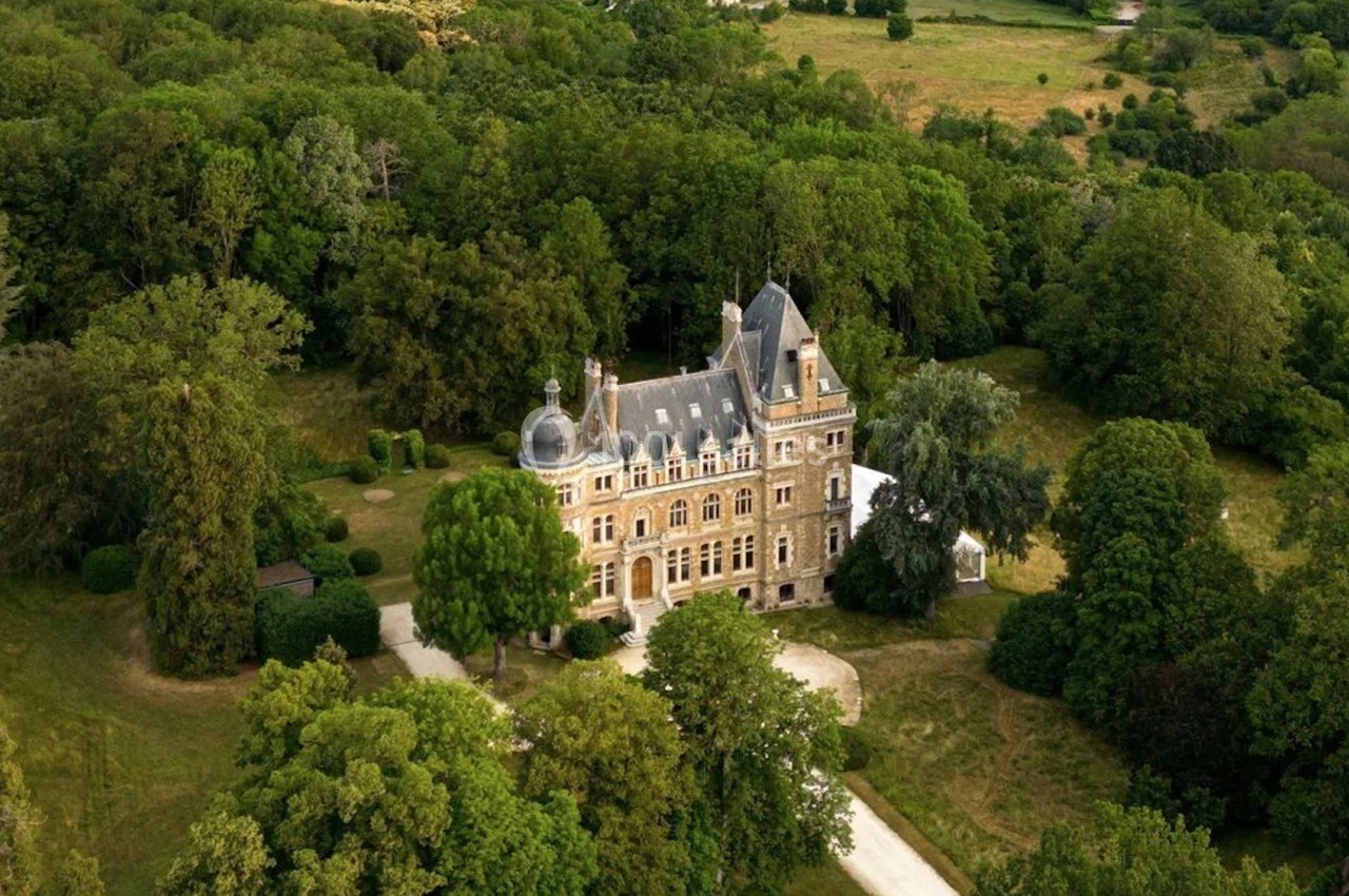 Vue aérienne d'un château entouré de vastes espaces verts et d'arbres dans un paysage rural.
