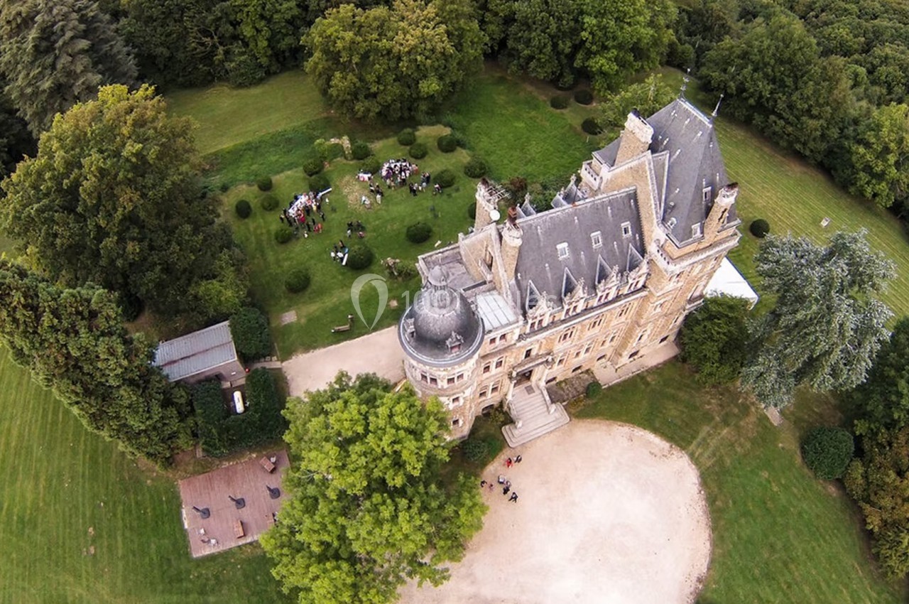 Vue aérienne d'un château entouré de jardins verdoyants avec des groupes de personnes rassemblés à l'extérieur.
