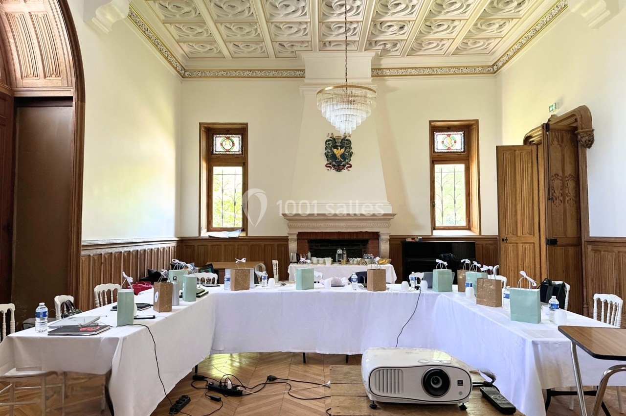 Salle de réunion lumineuse avec tables en U, matériel de présentation et décorations en bois et vitraux.