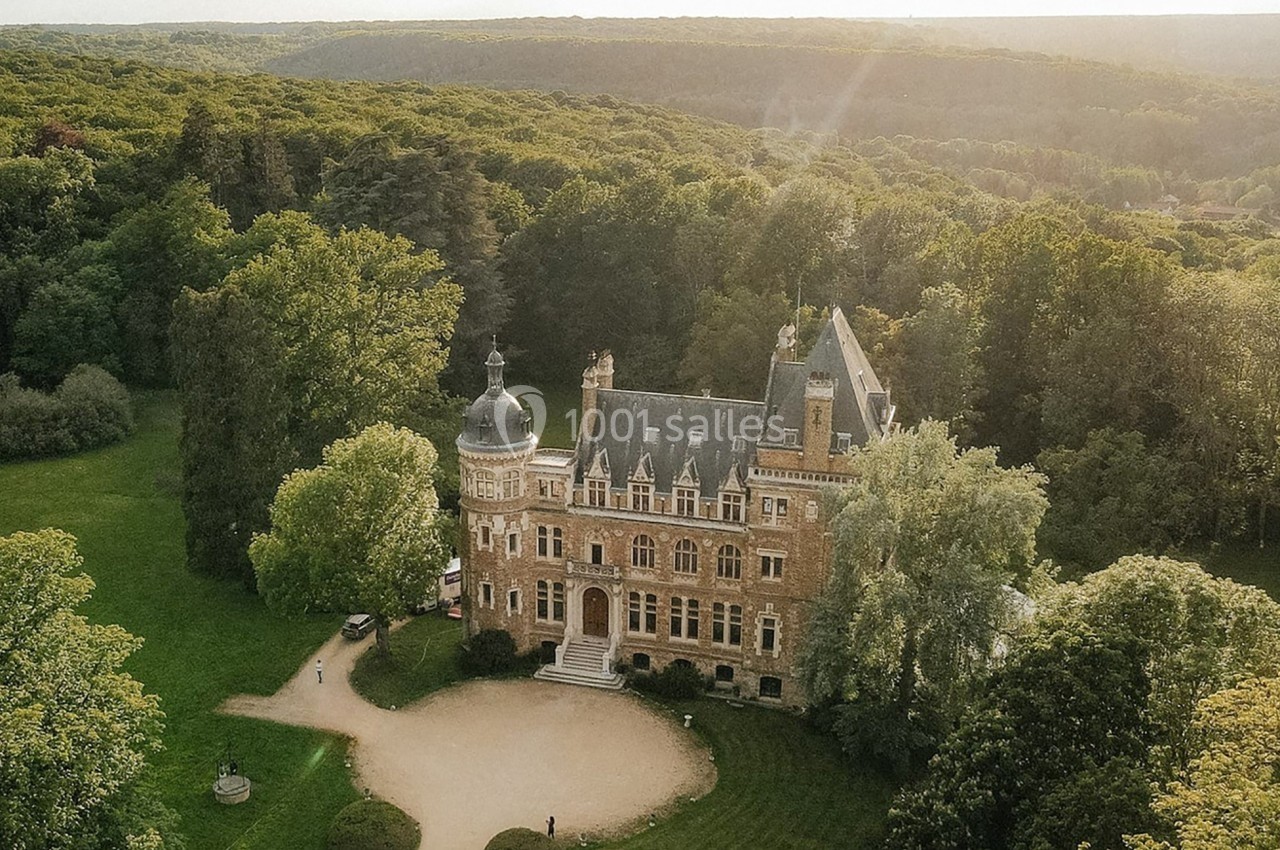 Vue aérienne d'un château entouré de vastes espaces verts et de forêts sous une lumière douce.