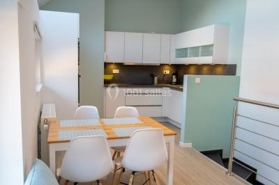 Salle de réception avec murs en briques, poutres apparentes, tables hautes et chaises pliantes sous des lampes suspendues.