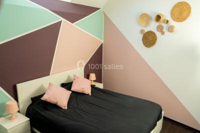 Salle de réception avec murs en briques, poutres apparentes, tables hautes et chaises pliantes sous des lampes suspendues.