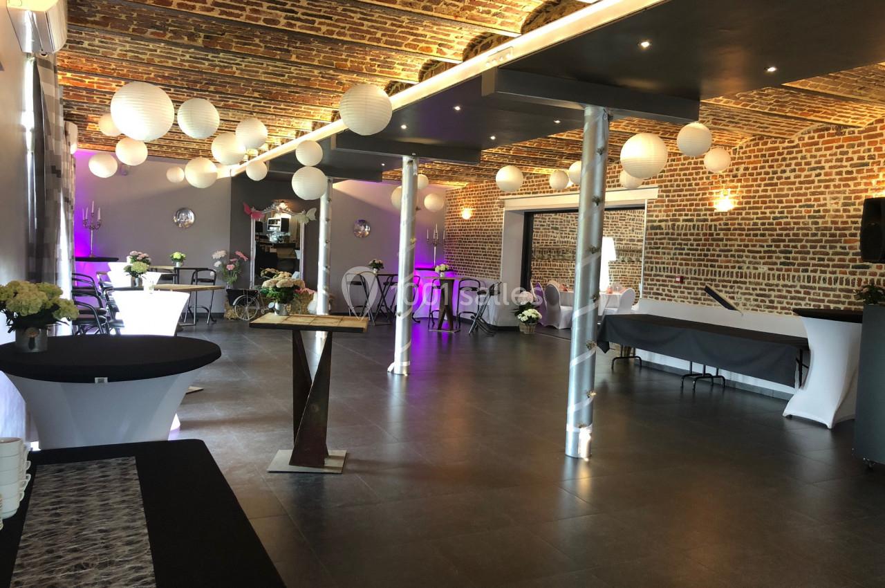 Salle de réception avec murs en briques, tables décorées et lanternes suspendues au plafond.