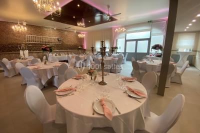 Salle de réception avec murs en briques, poutres apparentes, tables hautes et chaises pliantes sous des lampes suspendues.