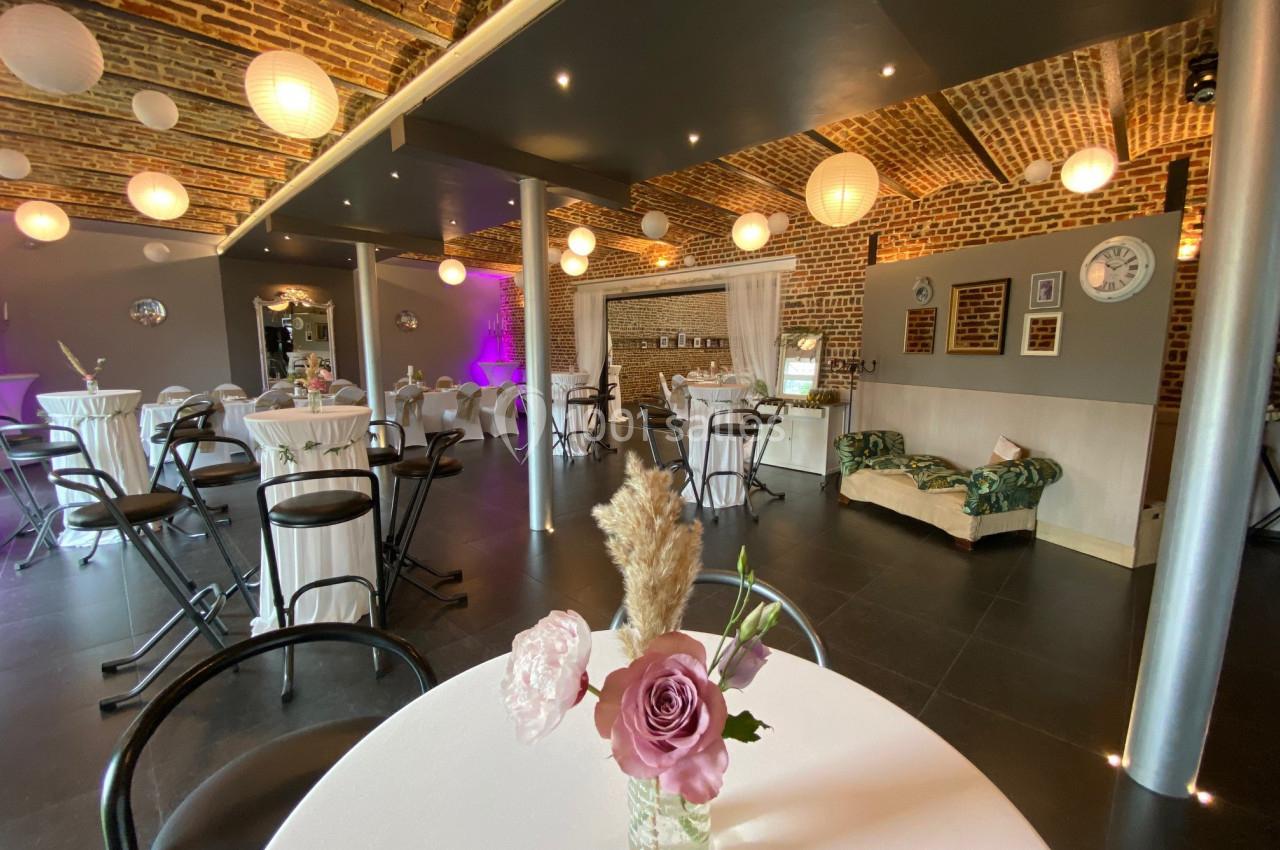 Salle de réception avec murs en briques, tables hautes décorées et éclairage tamisé, ambiance conviviale.