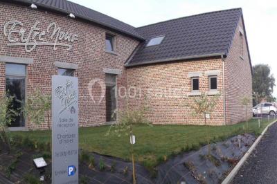 Salle de réception avec murs en briques, poutres apparentes, tables hautes et chaises pliantes sous des lampes suspendues.