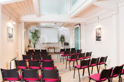 Salle de réunion avec table blanche, chaises rouges, écran mural et éclairage au plafond.