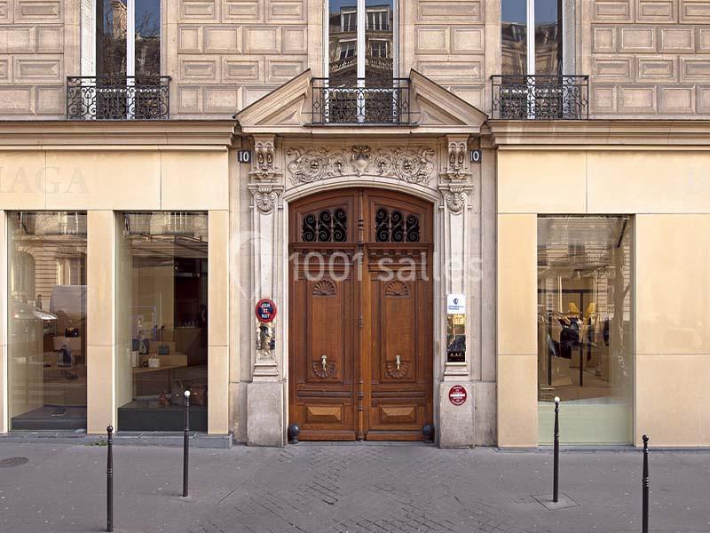 Façade d'un bâtiment avec une porte en bois sculptée, encadrée par des vitrines et des éléments architecturaux classiques.