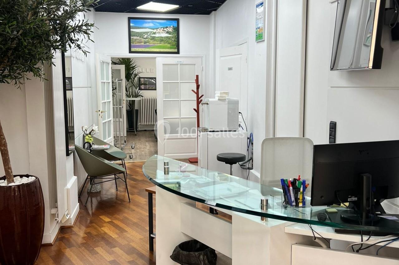 Bureau moderne avec comptoir en verre, mobilier blanc, sol en bois, et plantes décoratives dans un espace lumineux.