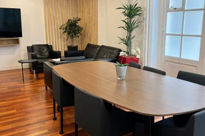 Salle de réunion avec table blanche, chaises rouges, écran mural et éclairage au plafond.