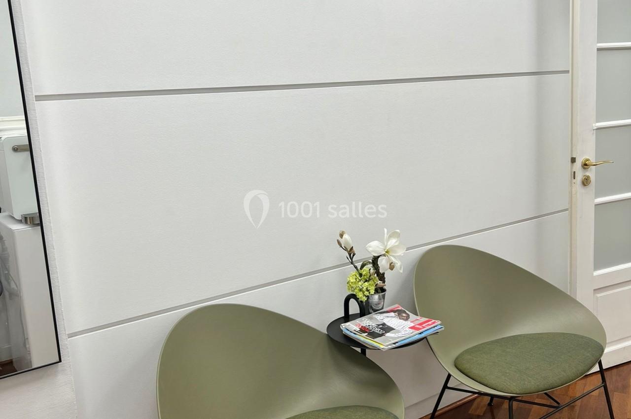 Deux fauteuils verts autour d'une petite table avec des magazines et une fleur, dans un espace lumineux marqué ’Espace…