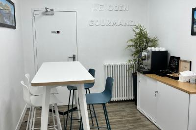 Salle de réunion avec table blanche, chaises rouges, écran mural et éclairage au plafond.