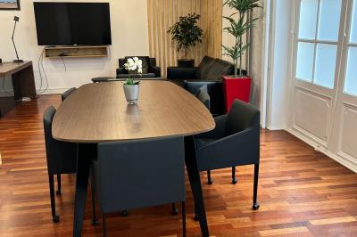 Salle de réunion avec table blanche, chaises rouges, écran mural et éclairage au plafond.