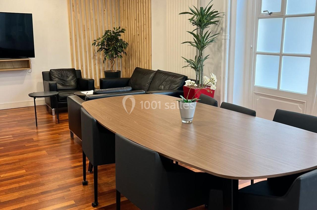 Salle lumineuse avec table en bois, chaises noires, canapé, plantes et parquet en bois.