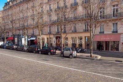 Salle de réunion avec table blanche, chaises rouges, écran mural et éclairage au plafond.