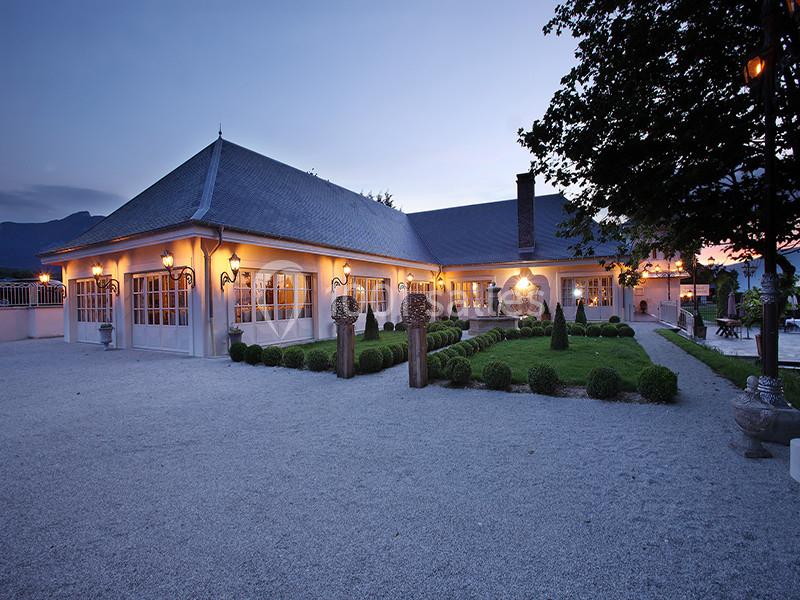 Grande maison éclairée au crépuscule, entourée d'un jardin soigné et d'une allée gravillonnée.