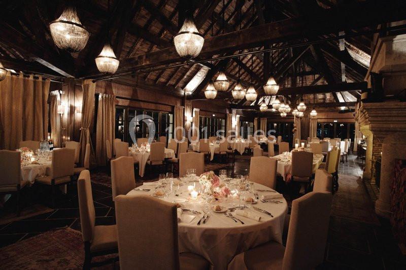 Salle de réception élégante avec tables rondes dressées, éclairée par des lustres et une lumière tamisée.