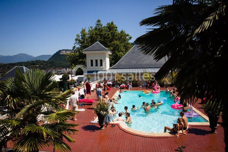 Personnes profitant d'une piscine extérieure entourée de palmiers et de montagnes sous un ciel dégagé.