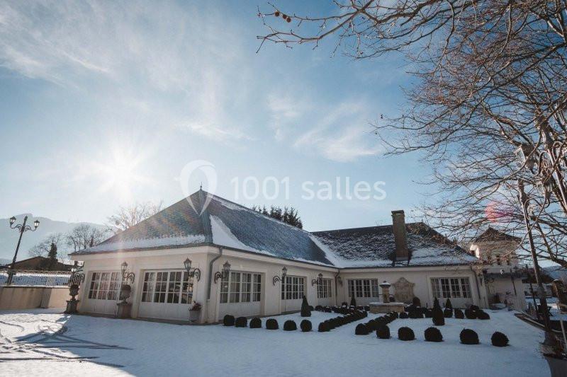 Bâtiment avec toit enneigé entouré d'arbres sous un ciel ensoleillé en hiver.