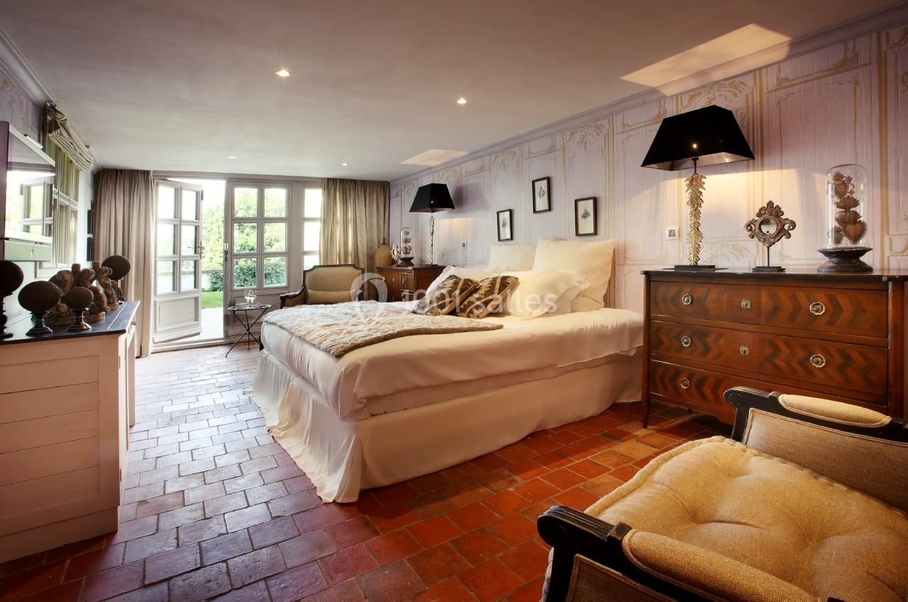 Chambre lumineuse avec lit double, mobilier classique, sol en terre cuite et vue sur un jardin par des portes-fenêtres.