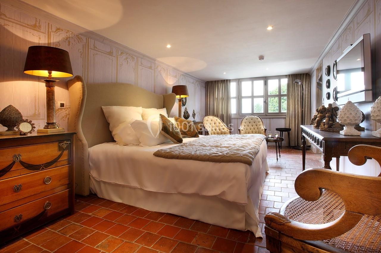 Chambre lumineuse avec lit double, mobilier en bois, lampes de chevet et sol en carrelage rouge.