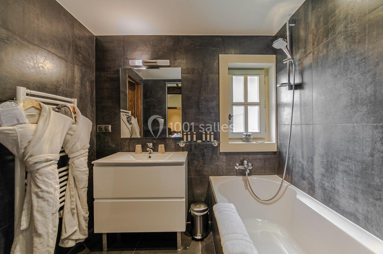 Salle de bain moderne avec baignoire, meuble lavabo, miroir, porte-serviettes et murs en carrelage sombre.