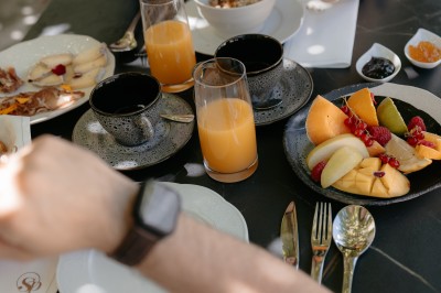 Deux personnes prennent un petit-déjeuner avec fruits, jus d'orange, céréales et couverts sur une table noire.