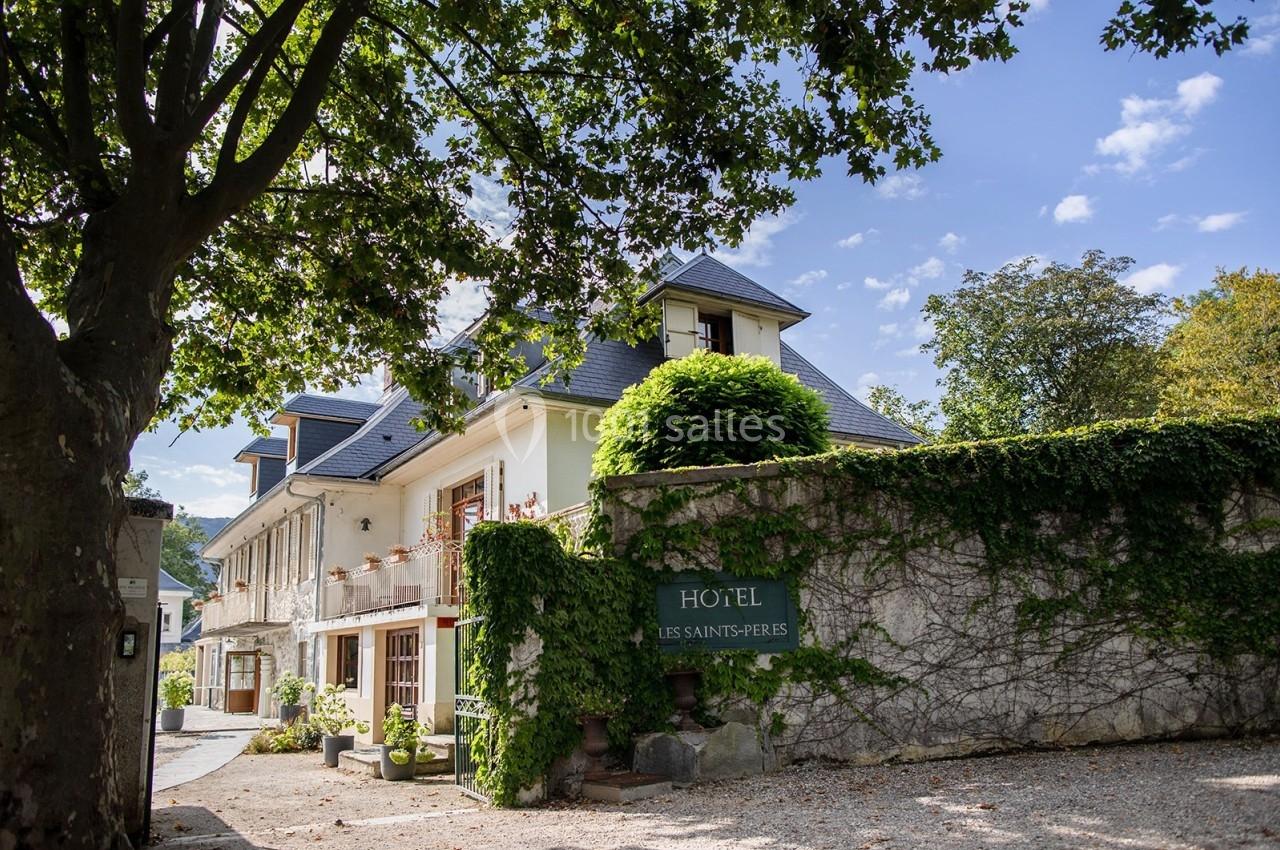 Façade d'un hôtel entouré de verdure, avec un mur en pierre partiellement couvert de lierre.