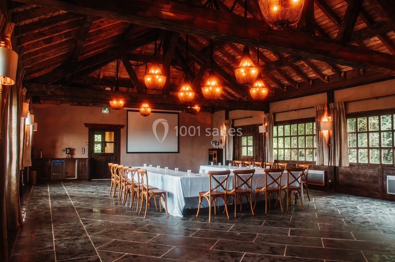 Salle de réunion avec une grande table rectangulaire entourée de chaises en bois, éclairée par des lustres suspendus.