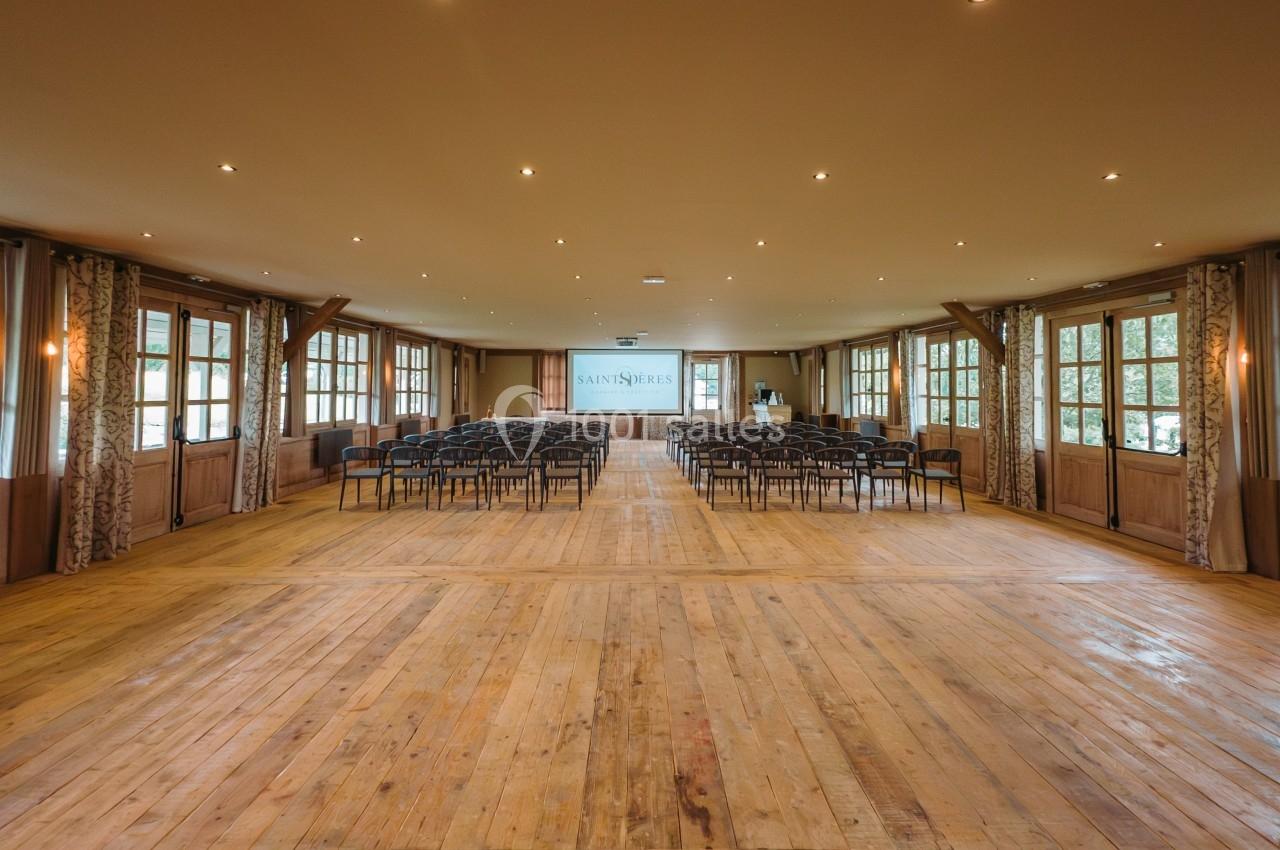 Salle lumineuse avec parquet en bois, rangées de chaises alignées face à un écran de projection.