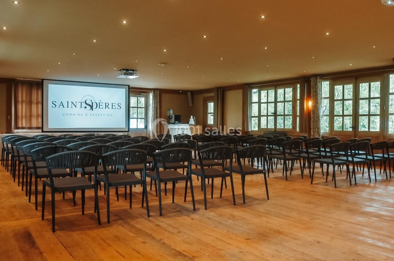 Salle de conférence lumineuse avec rangées de chaises noires, écran de projection et parquet en bois clair.
