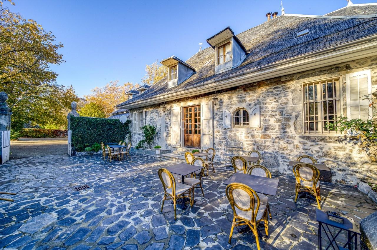 Cour pavée avec des tables et chaises en métal devant une maison en pierre sous un ciel bleu.