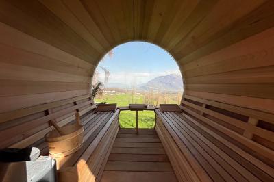 Intérieur d'un sauna en bois en forme de tonneau avec vue sur un paysage verdoyant et des montagnes au loin.