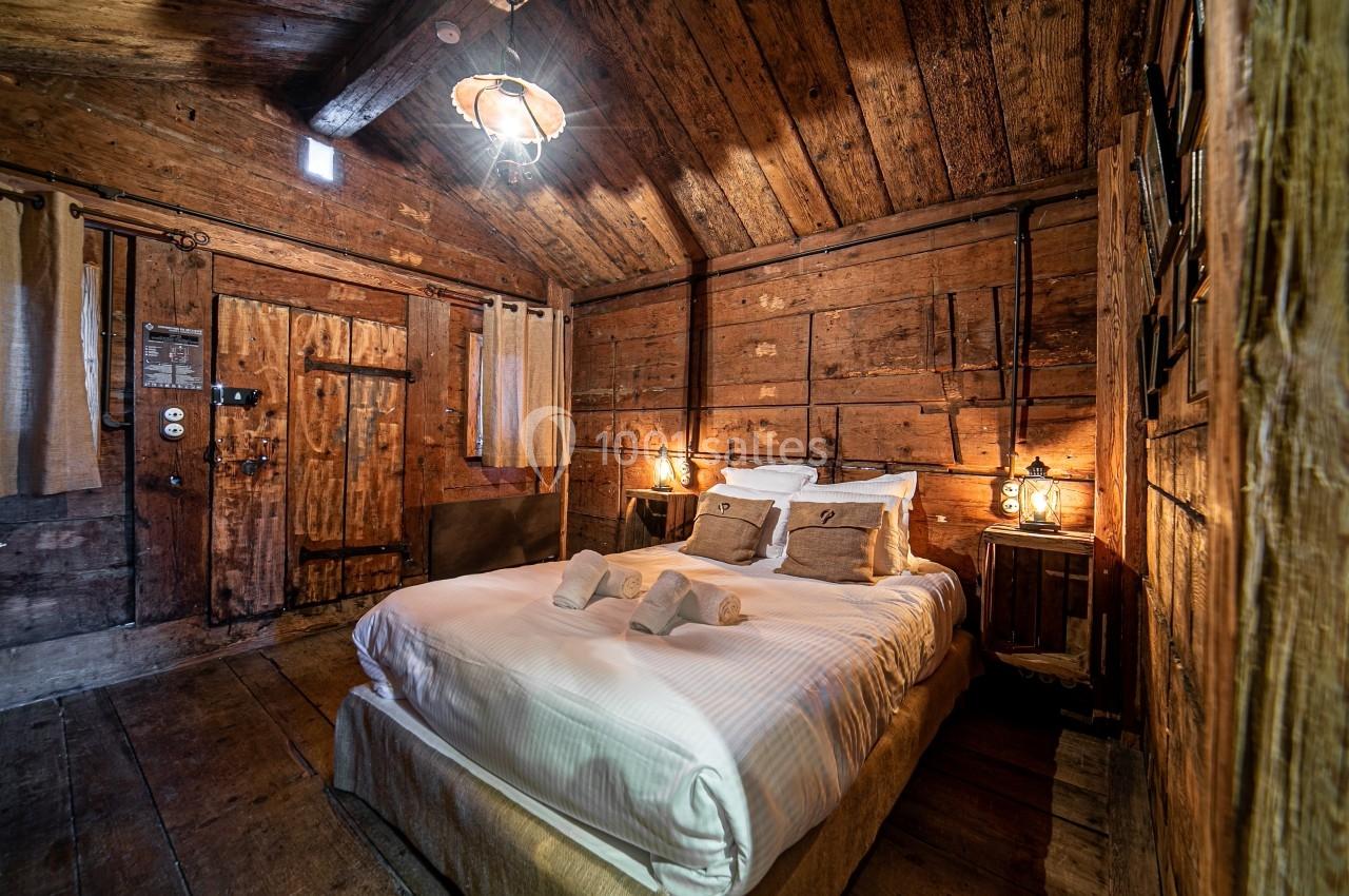 Chambre rustique en bois avec un lit double, des draps blancs, des lampes de chevet et une lumière chaleureuse.