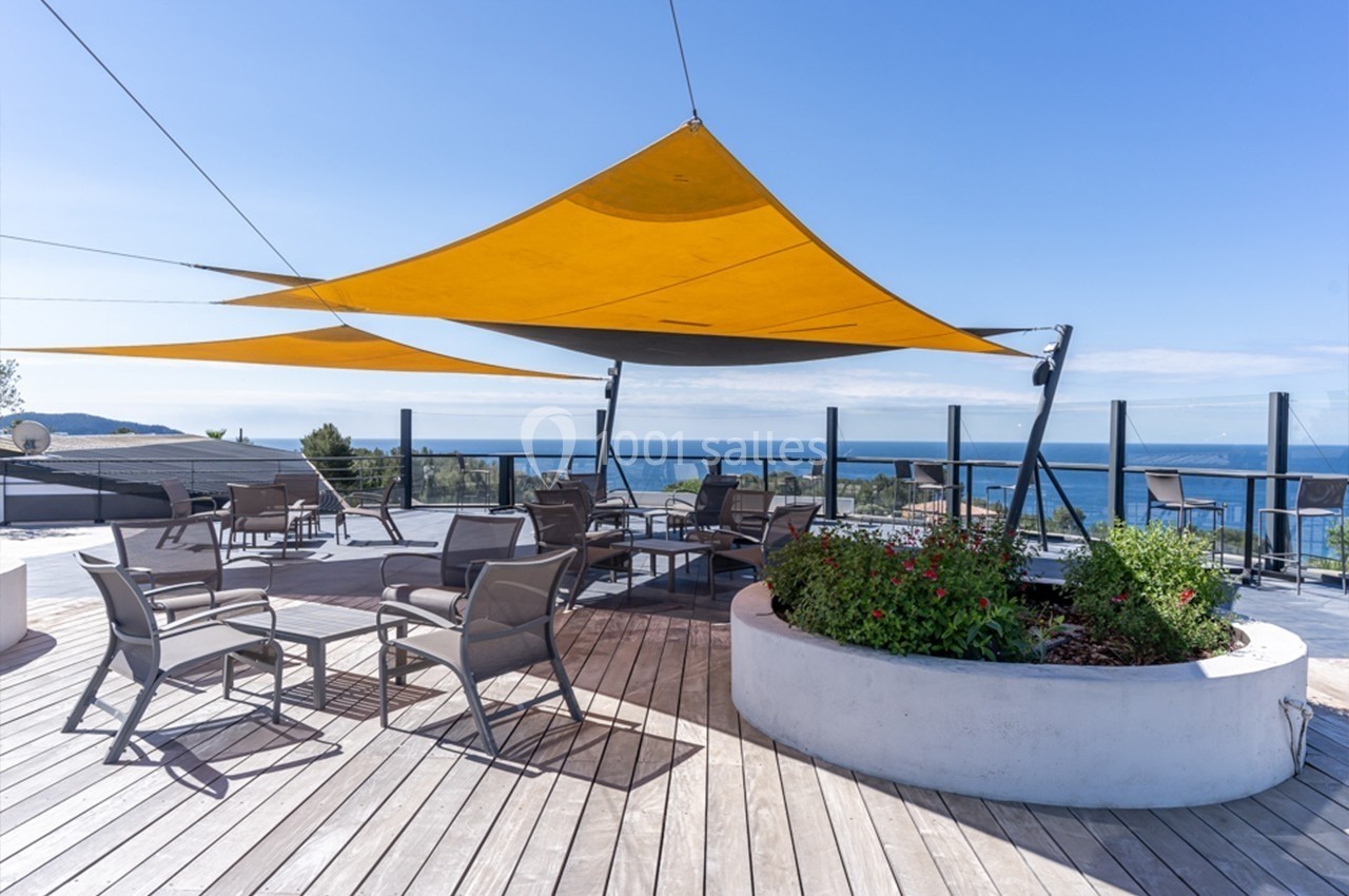 Terrasse en bois avec voiles d'ombrage jaunes, mobilier de jardin et vue dégagée sur la mer.