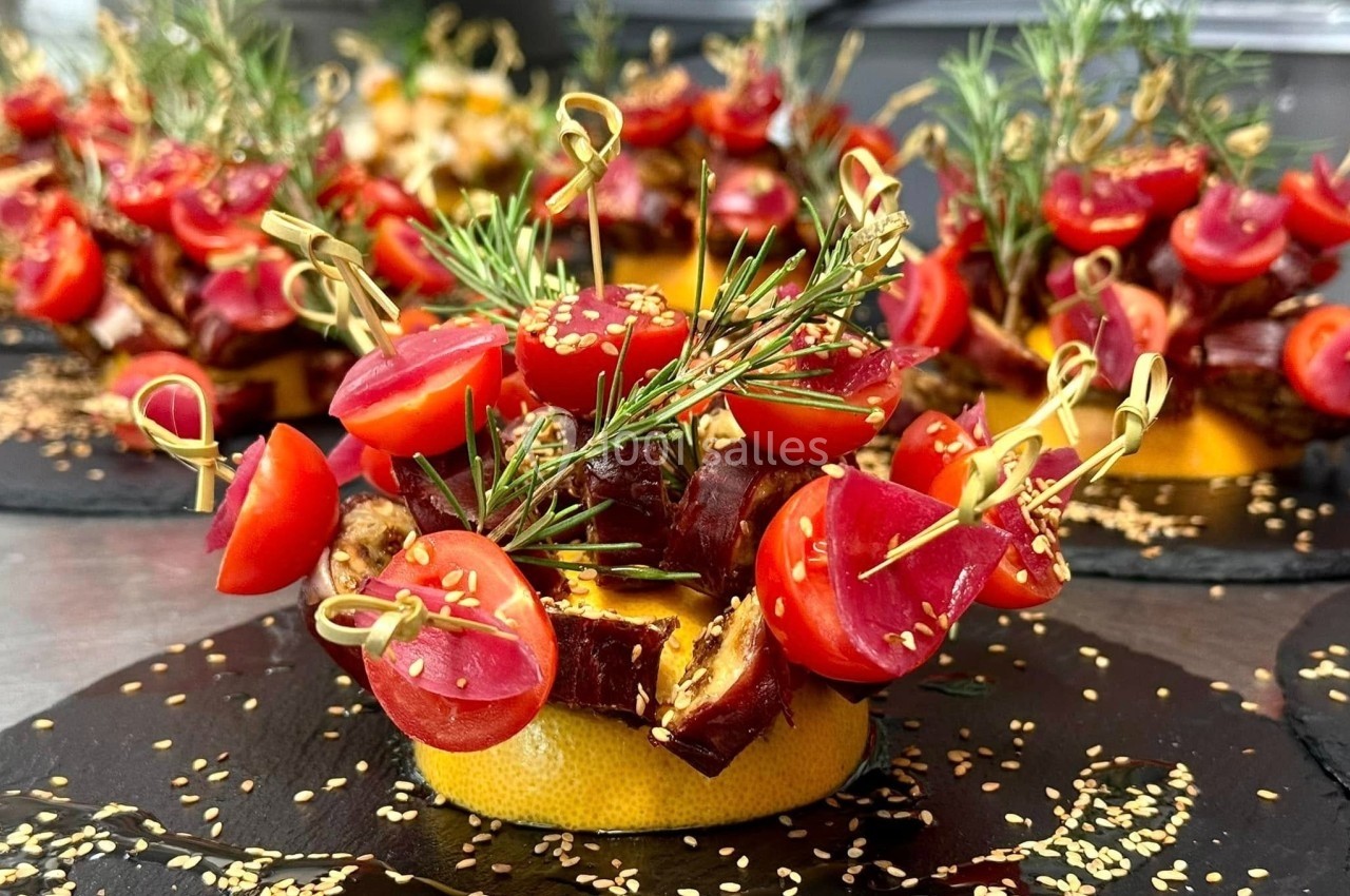 Assiette garnie de brochettes de tomates cerises, dattes et fromage, décorée de romarin et graines de sésame.
