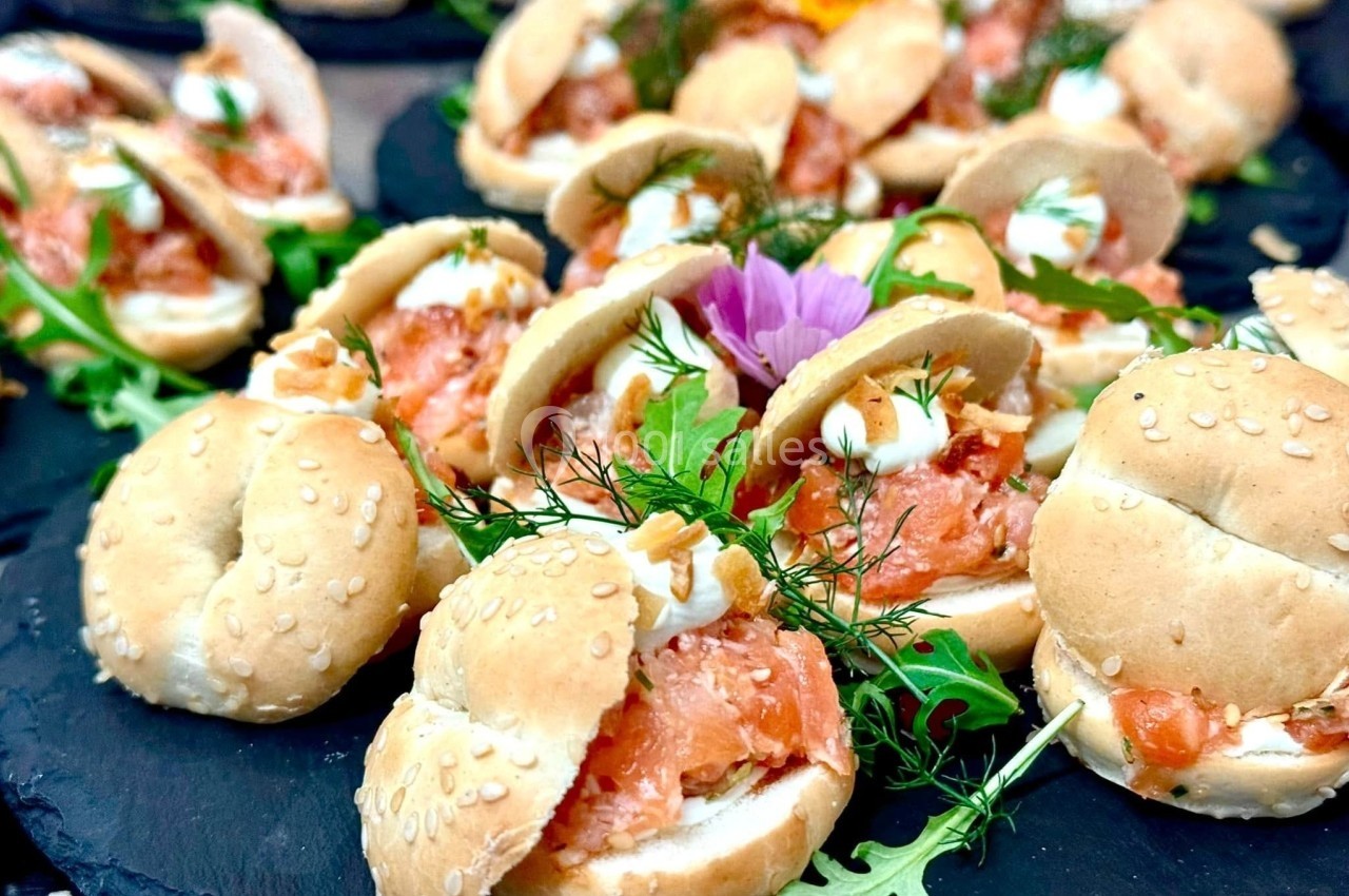 Mini-bagels garnis de saumon fumé, fromage frais et herbes, présentés sur un plateau avec de la roquette.
