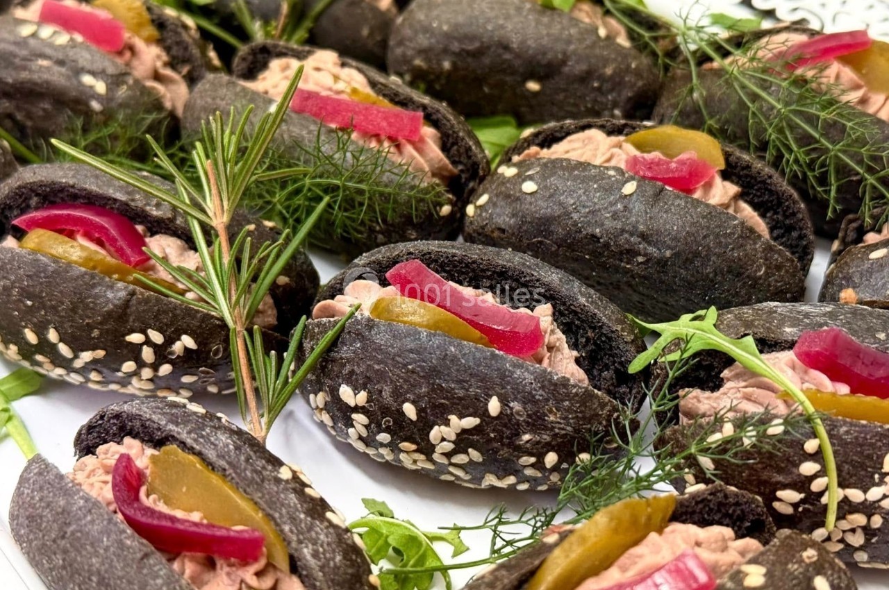 Mini pains noirs garnis de rillettes, cornichons, pickles rouges et décorés de graines de sésame et herbes fraîches.