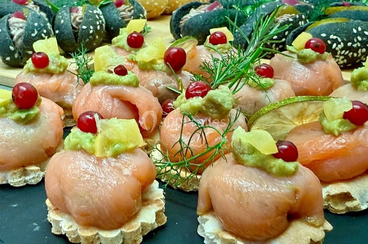 Assortiment de canapés au saumon fumé, garnis d'avocat, ananas, groseilles et herbes fraîches sur un plateau.