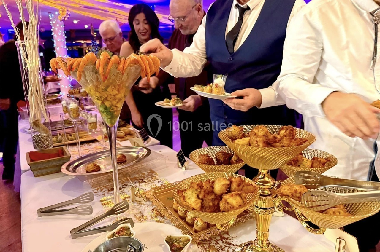 Buffet élégant avec verrine de crevettes et plats dorés, des convives se servant dans une ambiance festive.