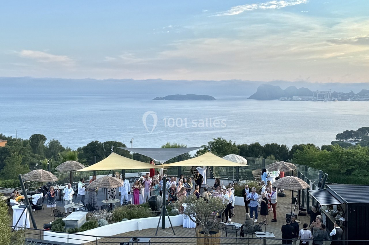 Groupe de personnes réunies sur une terrasse avec vue sur la mer et des collines à l'horizon.