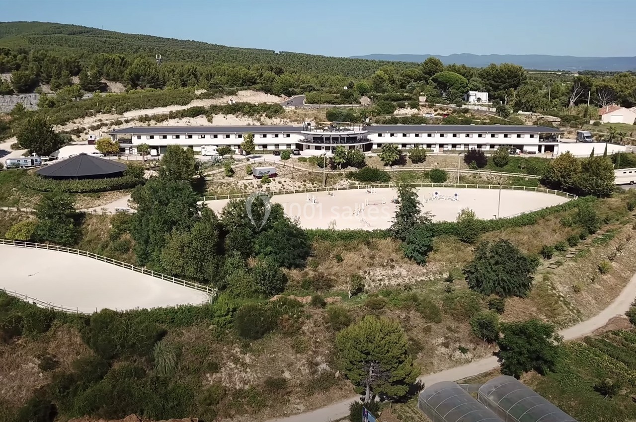 Vue aérienne d'un complexe équestre entouré de végétation et de collines, avec des carrières de sable visibles.