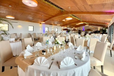 Salle de réception élégamment décorée avec des tables rondes dressées, nappes blanches et centres de table floraux.