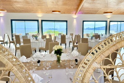 Salle de réception élégamment décorée avec des tables rondes dressées, nappes blanches et centres de table floraux.
