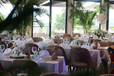 Salle de réception élégamment décorée avec des tables rondes dressées, nappes blanches et centres de table floraux.