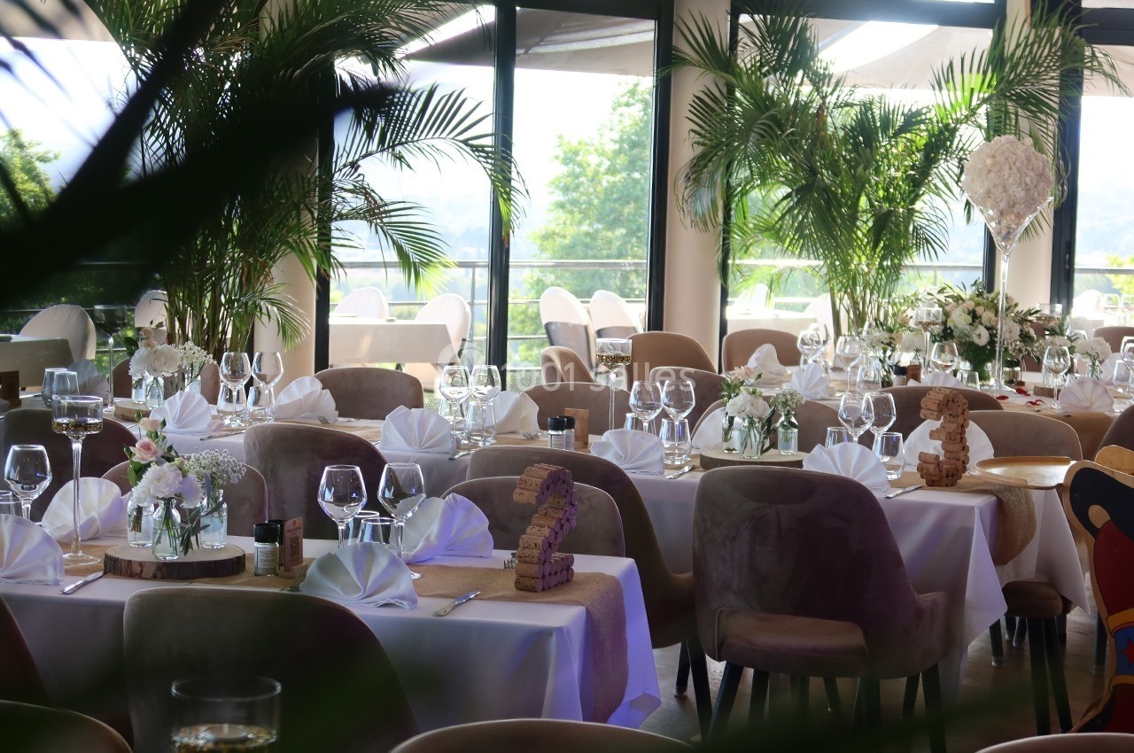 Salle de réception élégante avec tables dressées, nappes blanches, serviettes pliées et décorations florales.