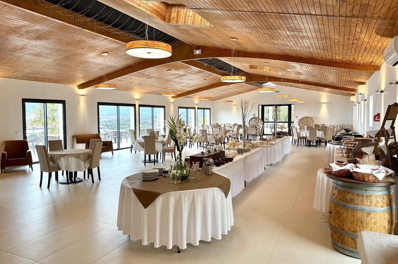 Salle lumineuse avec tables dressées, buffet central et plafond en bois, offrant une vue panoramique à travers de grandes…
