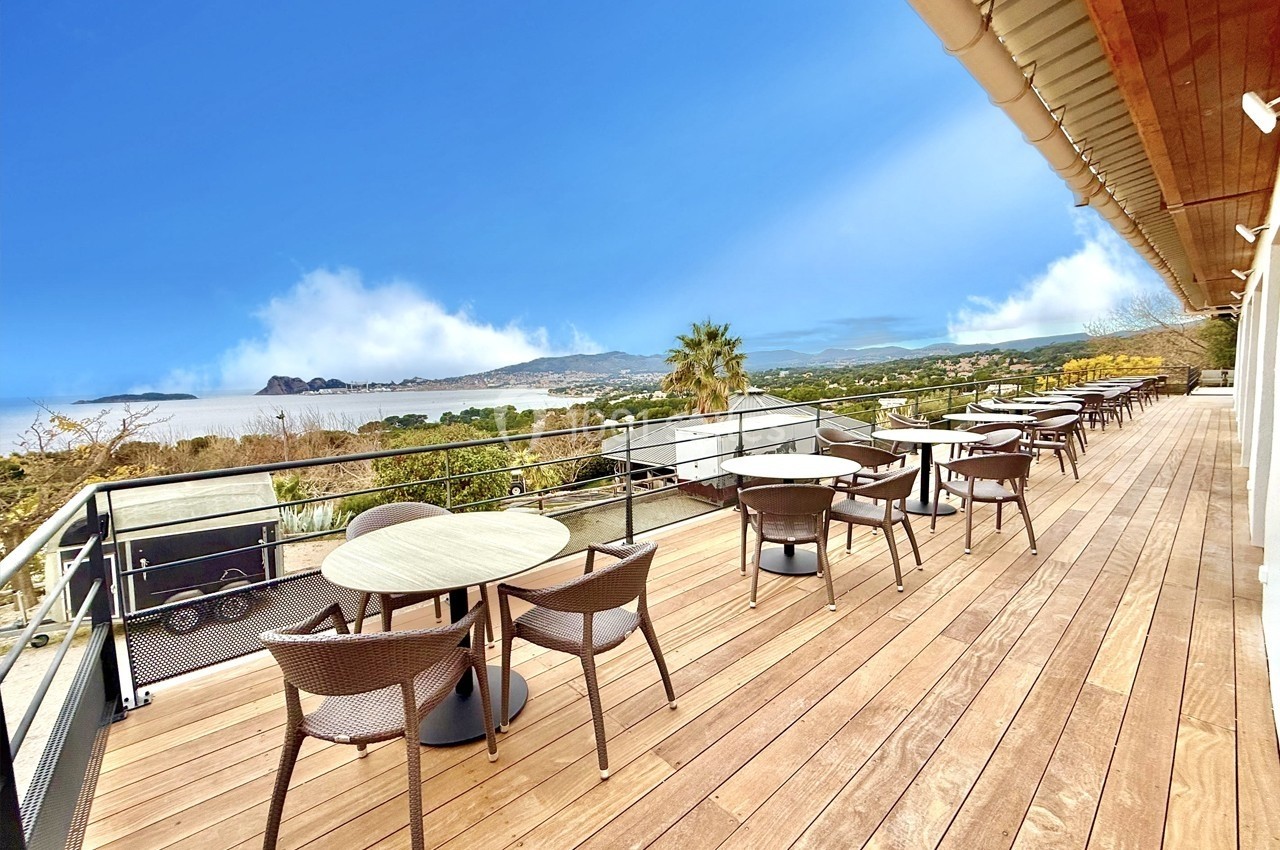 Terrasse en bois avec tables et chaises, offrant une vue dégagée sur un paysage naturel et un ciel bleu.